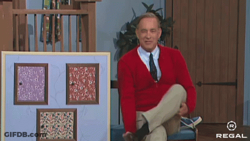 Man In Red Sweater And Tie Sitting In Front Of Regal Sign GIF