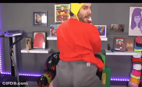 Man In Red Sweater And Yellow Hat Standing In Room With Pictures GIF