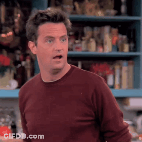 Man In Red Sweater Standing In Front Of Shelf Making Funny Face GIF