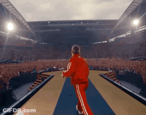 Man In Red Tracksuit Walking Into Crowded Stadium GIF