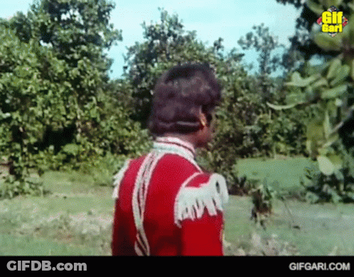 Man In Red Uniform Standing In Grassy Field GIF