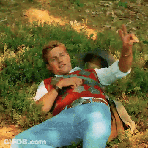 Man In Red Vest And Blue Jeans Laying In Grass GIF