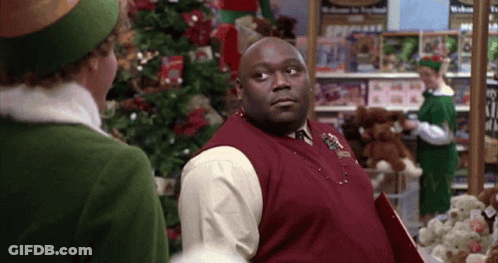 Man In Red Vest Next To Woman In Green Hat In Front Of Christmas Tree GIF