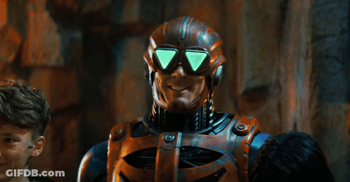 Man In Robot Costume Standing In Front Of Here's Sign GIF