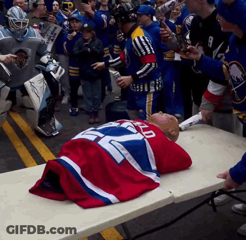 Man In Sabres Jersey Laying On Table Surrounded By Fans GIF