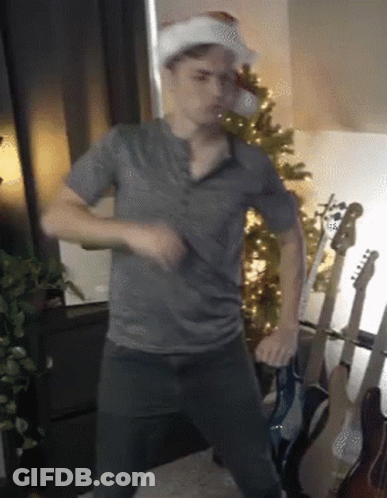 Man In Santa Hat Dancing By Christmas Tree GIF