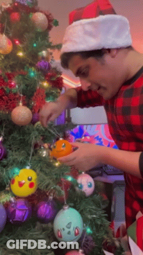 Man In Santa Hat Decorates Christmas Tree GIF