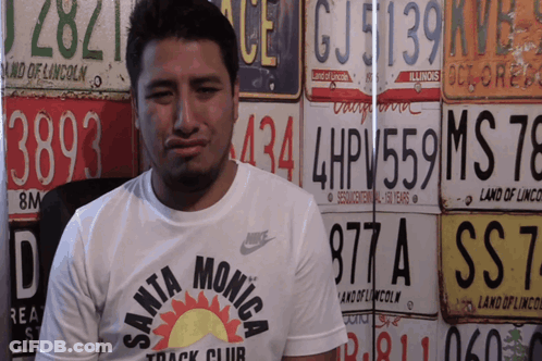 Man In Santa Monica Track Club Shirt In Front Of License Plates GIF