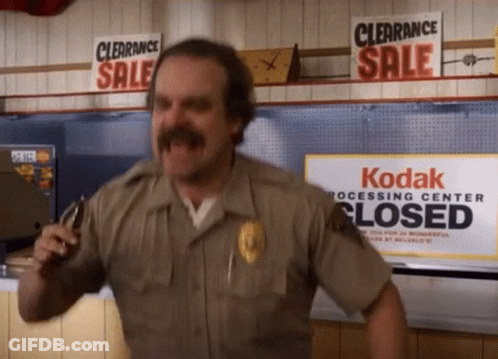 Man In Sheriff Uniform In Front Of Kodak Processing Center Sign GIF