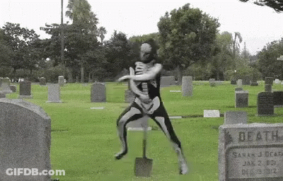 Man In Skeleton Costume Holding Shovel In Cemetery GIF