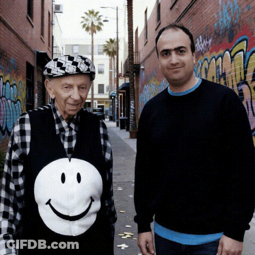 Man In Smiley Face Vest Beside Older Man GIF