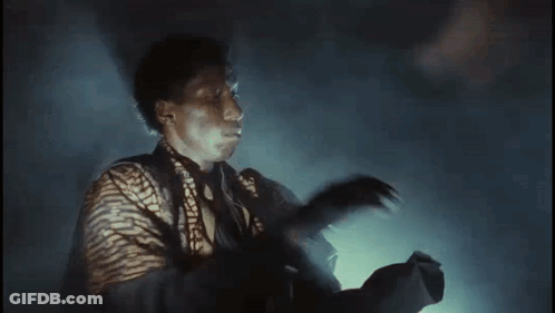 Man In Striped Shirt Holding Gun In Dark Room GIF