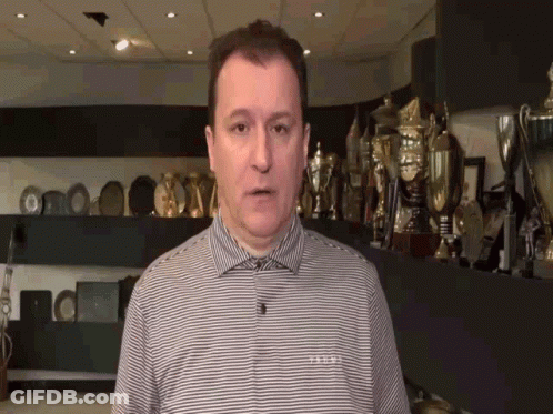 Man In Striped Shirt In Front Of Trophy Wall GIF