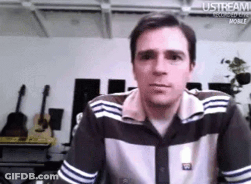 Man In Striped Shirt Sitting At Table Looking At Camera GIF
