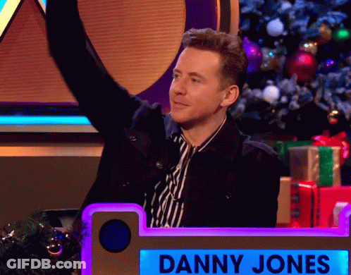 Man In Striped Shirt Standing Before Danny Jones Sign GIF