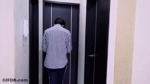 Man In Striped Shirt Standing In Front Of Black Door GIF