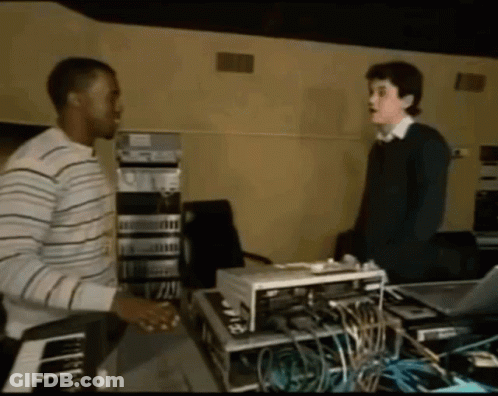 Man In Striped Shirt Talking To Another Man In Dark Room GIF