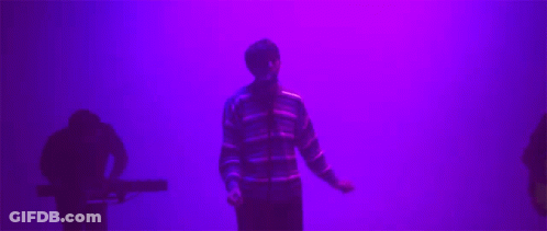 Man In Striped Sweater In Front Of Purple Wall GIF