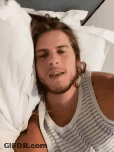 Man In Striped Tank Top Laying On White Sheets GIF