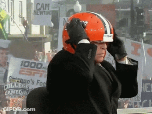 Man In Suit Adjusts Helmet In Front Of Cam Newton Sign GIF