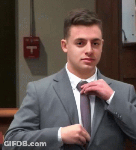 Man In Suit Adjusts Tie By Fire Extinguisher GIF