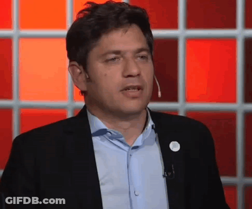 Man In Suit And Blue Shirt Talking Into Microphone In Front Of Red Wall GIF