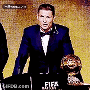 Man In Suit And Bow Tie Holding Trophy At Podium GIF