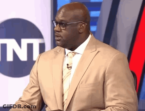 Man In Suit And Bow Tie Sitting In Front Of SNL Sign GIF