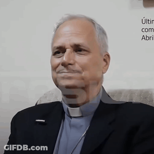 Man In Suit And Clergy Collar Smiling In Front Of Una Com Abri Sign GIF