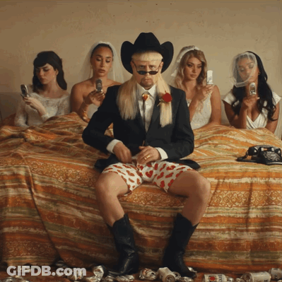 Man In Suit And Cowboy Hat On Bed Surrounded By Women GIF