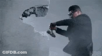 Man In Suit And Goggles Breaking Wall With Hammer GIF