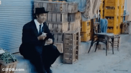 Man In Suit And Hat Sitting On Ledge Eating GIF
