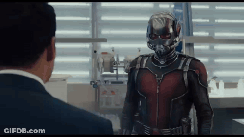 Man In Suit And Helmet Talking To Superhero GIF