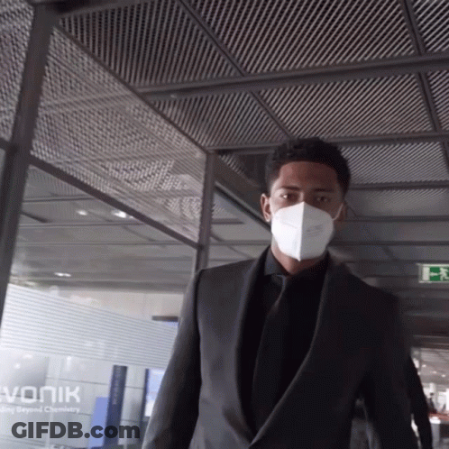 Man In Suit And Mask Walking Past Vonik Sign GIF