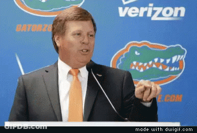 Man In Suit And Orange Tie At Podium With Verizon Logo GIF