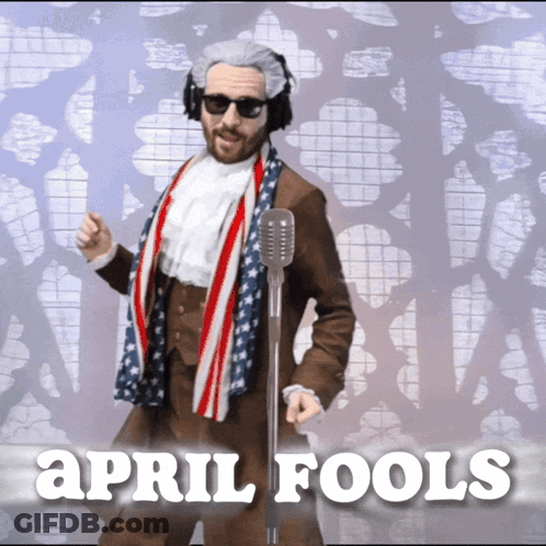 Man In Suit And Scarf At Microphone Saying April Fools GIF