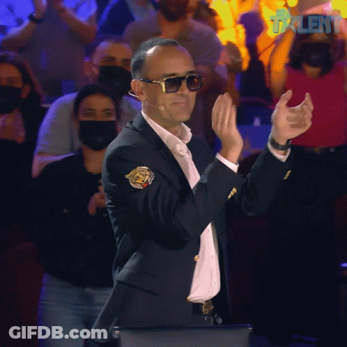 Man In Suit And Sunglasses Applauding In Front Of Masked Crowd GIF