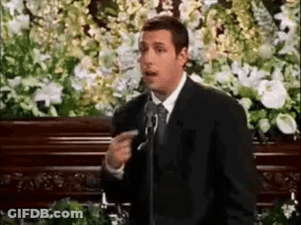 Man In Suit And Tie At Microphone In Front Of Coffin GIF