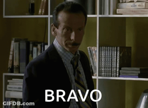 Man In Suit And Tie By Bookshelf With Bravo GIF