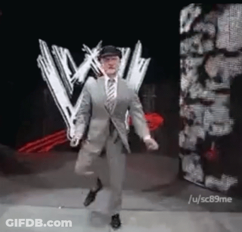 Man In Suit And Tie Dancing In Front Of Wrestling Logo GIF