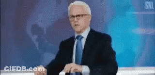 Man In Suit And Tie Facing Skull On Screen GIF