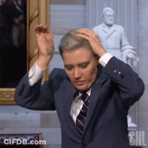Man In Suit And Tie Holding Head Next To SNL Statue GIF