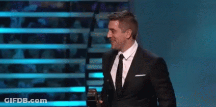 Man In Suit And Tie Holding Microphone On Stage GIF