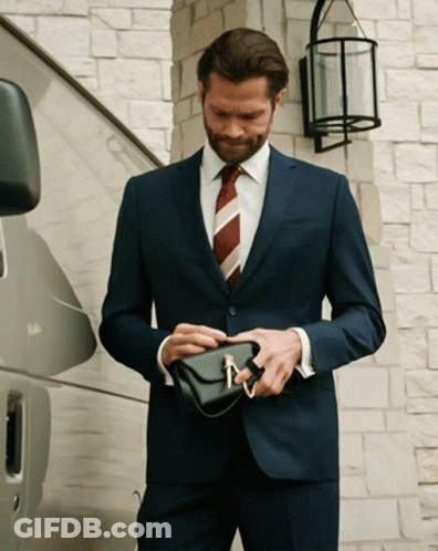 Man In Suit And Tie Holding Small Black Purse GIF