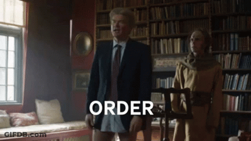 Man In Suit And Tie In Front Of Bookshelf Saying Order GIF
