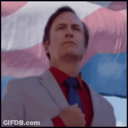 Man In Suit And Tie In Front Of Transgender Flag GIF