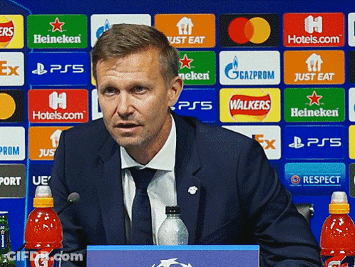 Man In Suit And Tie In Front Of Walkers Logo Wall GIF