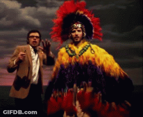 Man In Suit And Tie Next To Feathered Costume GIF