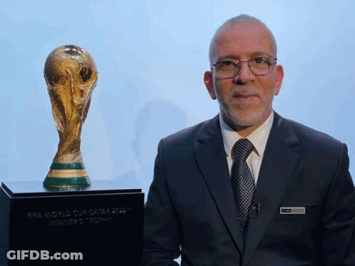 Man In Suit And Tie Next To FIFA World Cup Qatar 2022 Winner's Trophy GIF