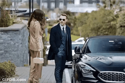 Man In Suit And Tie Next To Woman With Purse GIF